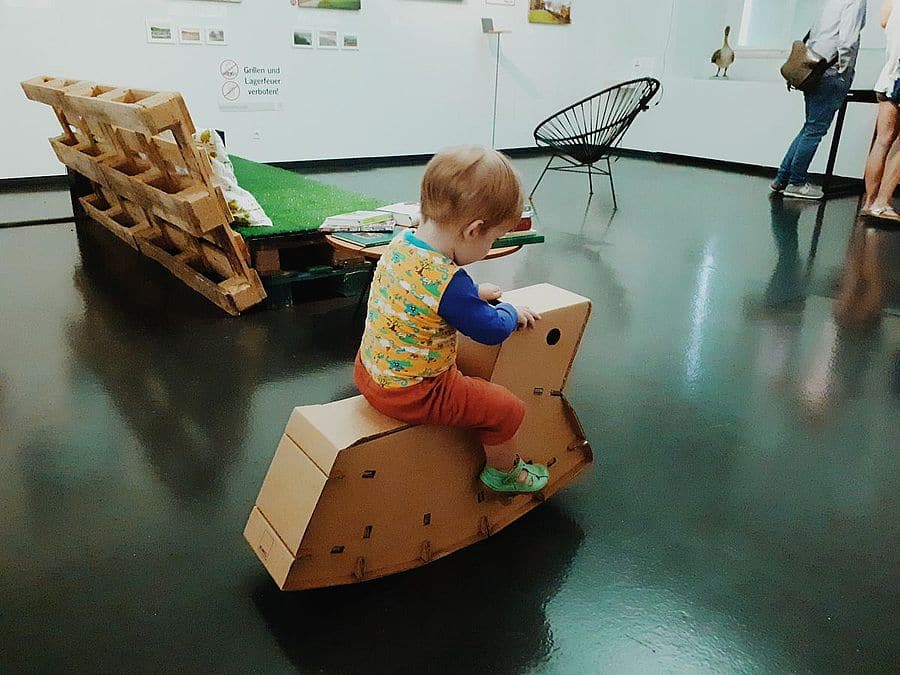 Unser Sohn auf dem Karton Schaukelpferd in der Ausstellung Stadtoasen im NORDICO Stadtmuseum in Linz